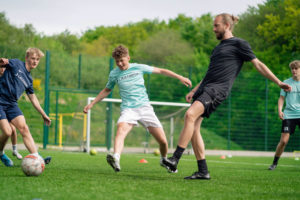 Fodboldtræner og to elever spiller fodbold på Lægårdens idrætsefterskole