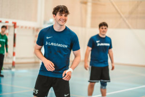 To drenge i en sportshal står og smiler og er i gang med en håndboldtræning