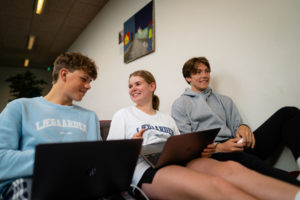 3 unge mennesker sidder med deres computere og snakker om skolearbejdet