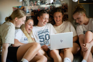 5 piger sidder og kigger på en computerskærm og griner.